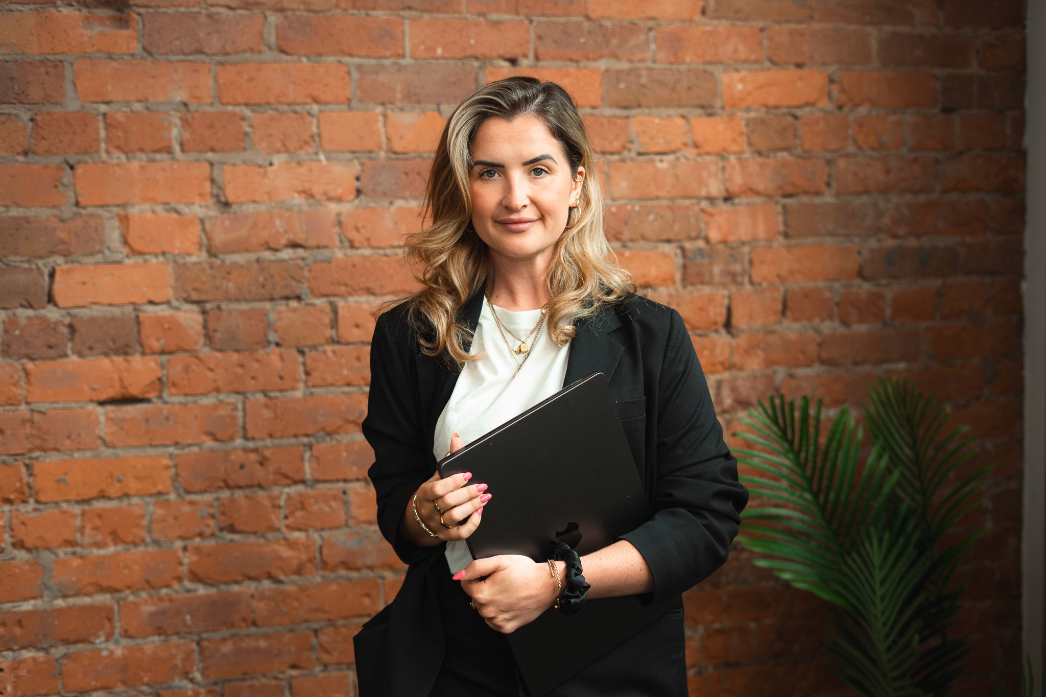 A PSS Tax adviser holding a laptop against the exposed brick wall of the Manchester office