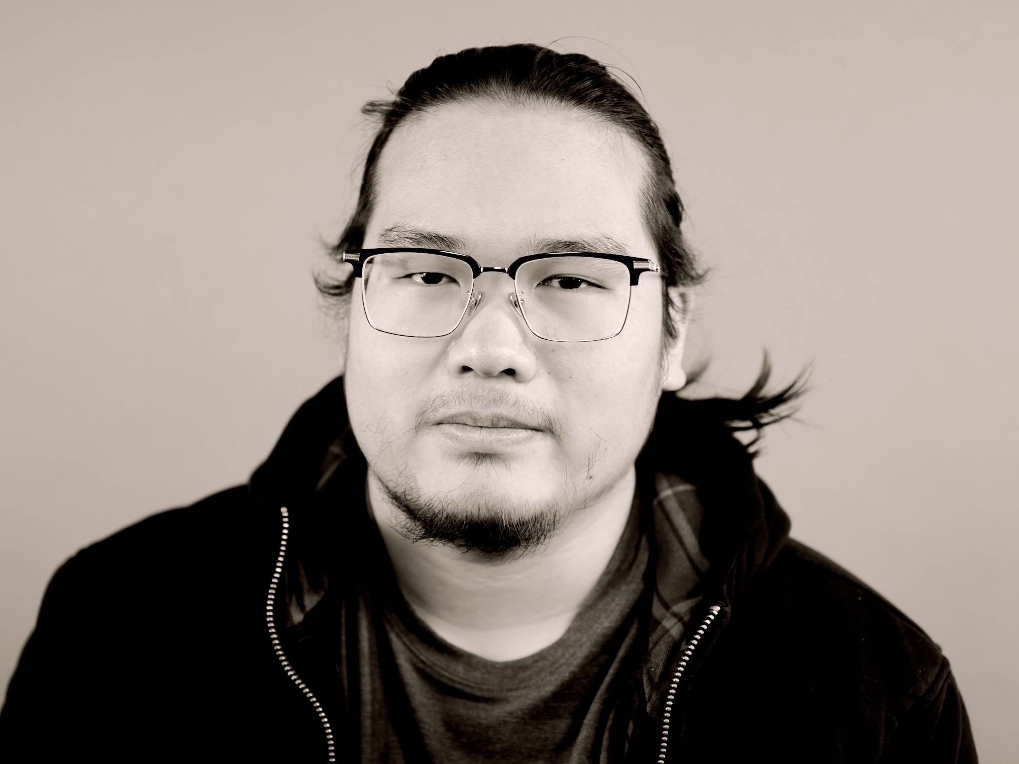 A thoughtful young person with dark hair gazes to the side, captured in soft black and white lighting.