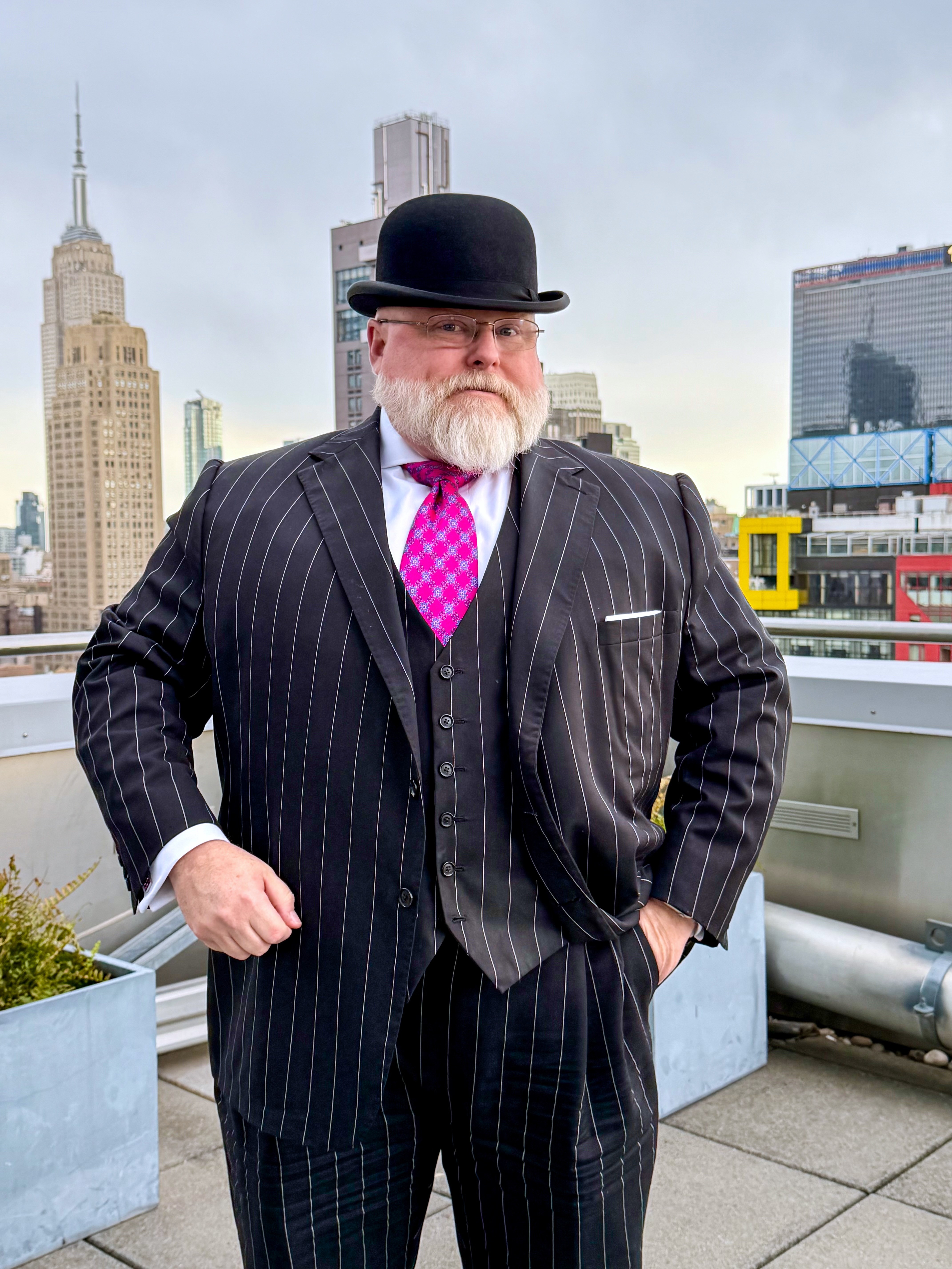 Dan Newman in a bowler hat, magenta tie, and black pinstripe three-piece suit.