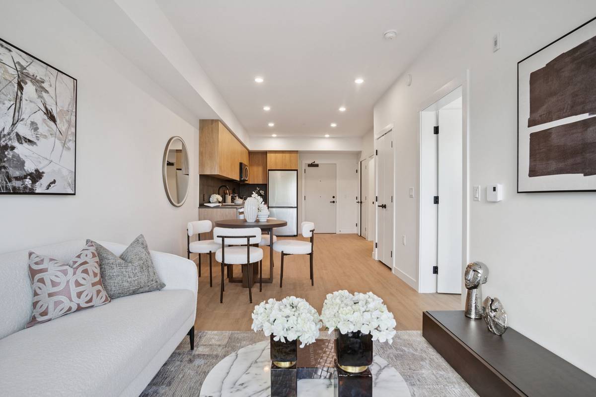 A bright, modern living area featuring a white sofa, coffee table, and open kitchen in the background.