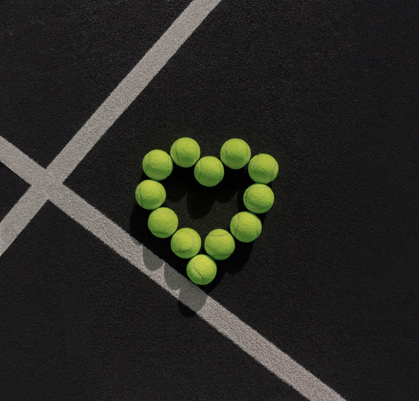 Mehrere gelbe Padelbälle formen ein Herz auf dem schwarzen Court mit weißen Linien – Symbol für Leidenschaft, Design und Community bei Padelnero.
