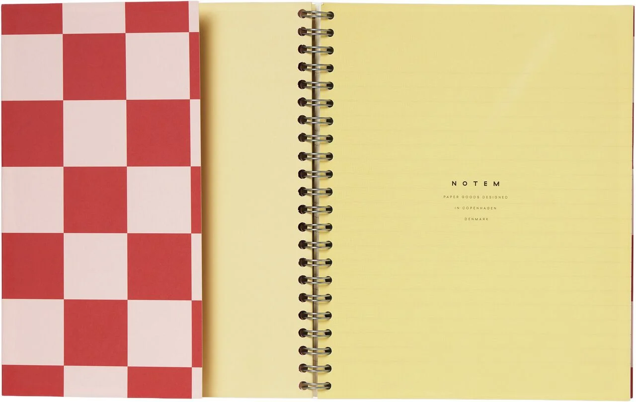 Notem Nela notebook shown open, with a red checkerboard cover and yellow spiral-bound lined pages.