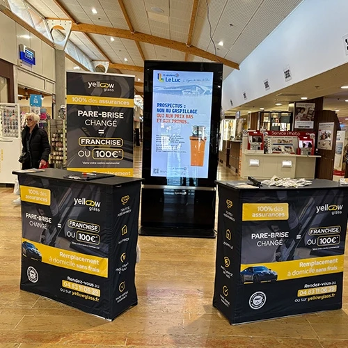 Publicité Yellow Glass : Remplacement Pare-Brise, franchise ou 100€. Stands d'information et affichage numérique dans un centre commercial.