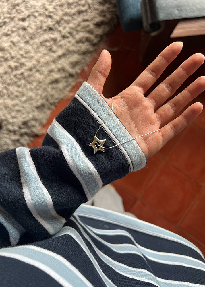 Hand wearing a star-shaped pendant necklace with a striped sleeve on a wooden floor.