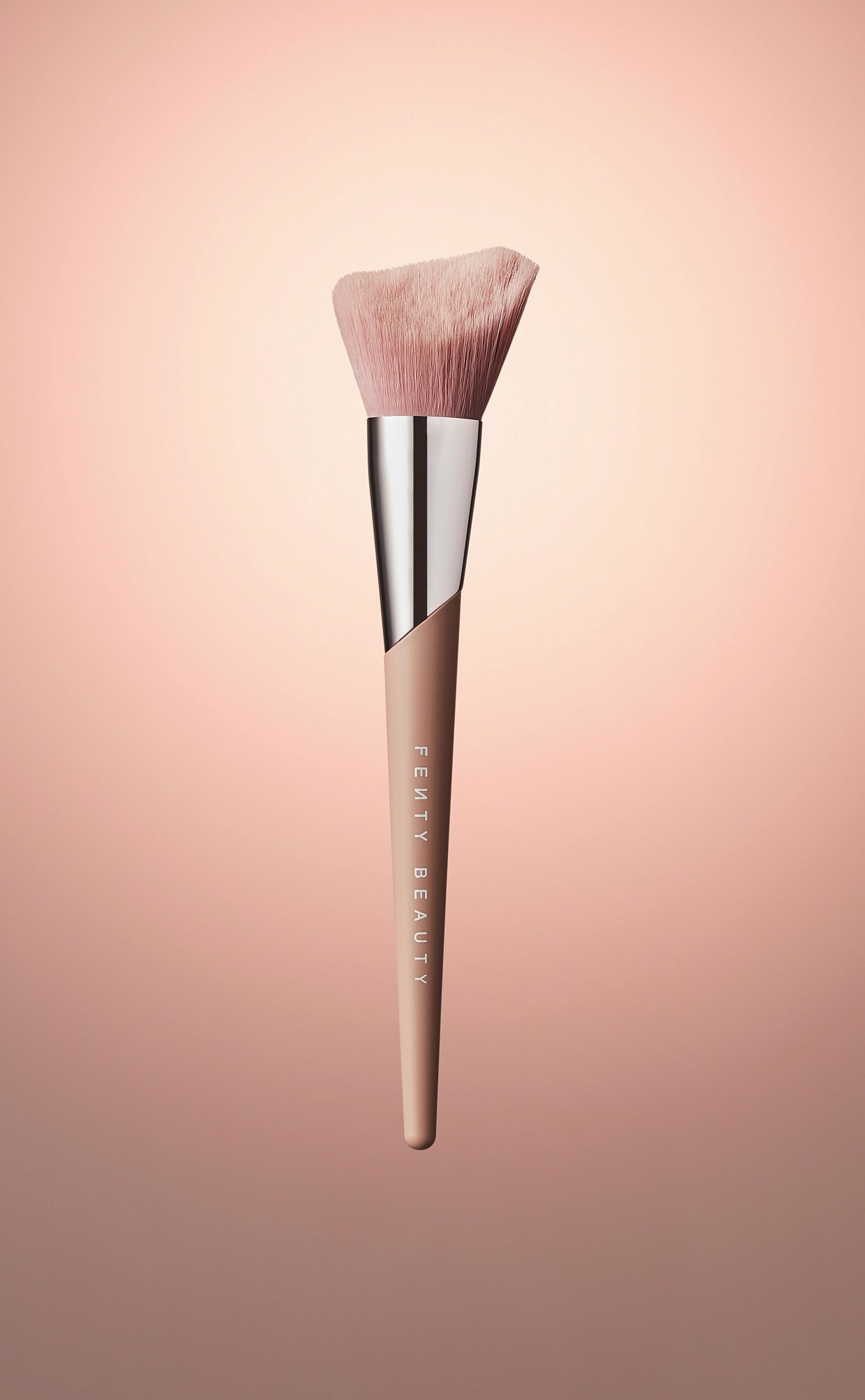 Makeup brush with a geometric-shaped head and a wooden handle, displayed against a soft pink background.