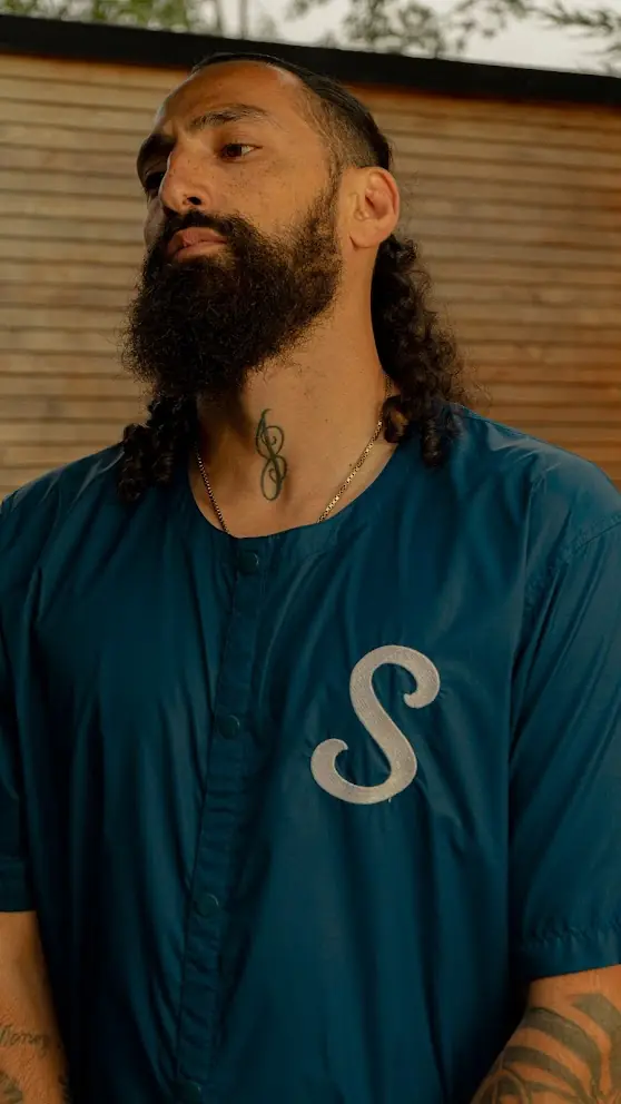 A man in a blue shirt stood up outside in front of a wooden fence.