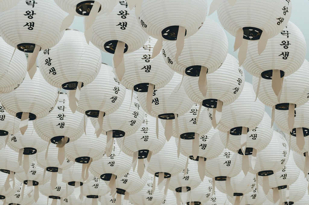 An array of white paper lanterns adorned with black Korean calligraphy hang closely together, creating an intricate and serene pattern against the sky, typical of traditional celebrations and festivals.