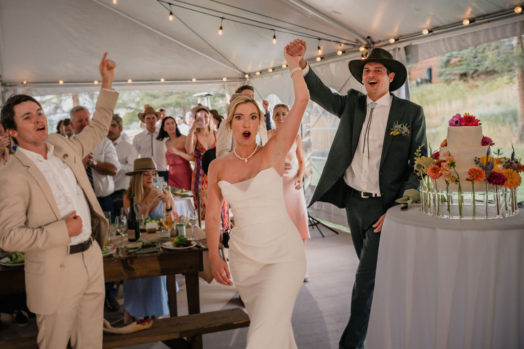 Newlyweds cheering together beside their wedding cake