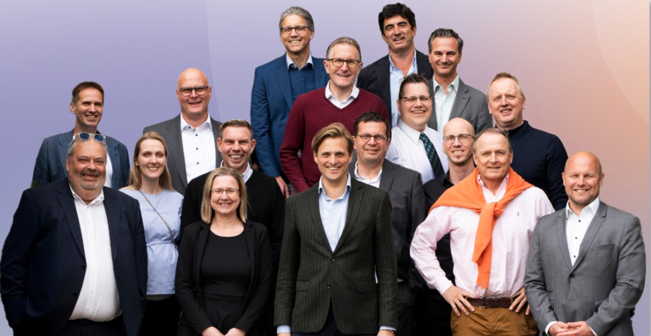 A person with dreadlocks wearing a mustard yellow sweater pulls the collar up to their nose, creating a cozy and mysterious atmosphere against a neutral background.