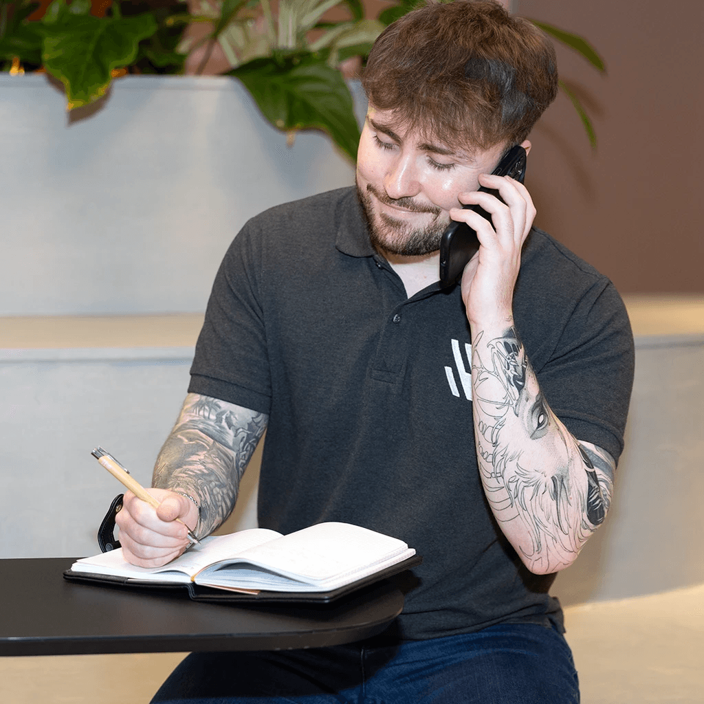 Jamie at a table on the phone, writing in a book
