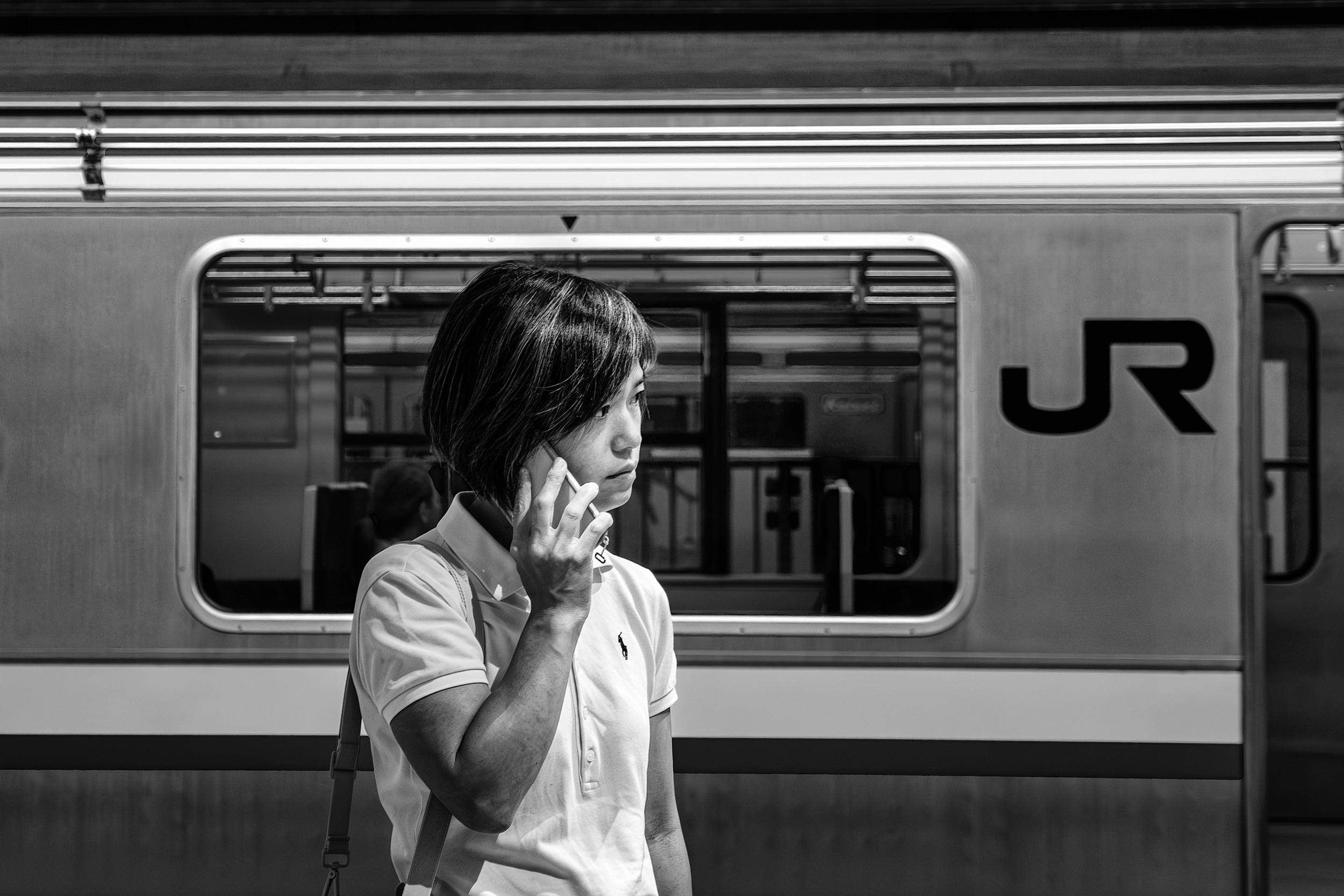 Black and white photograph of a person on their phone standing in front of a train.