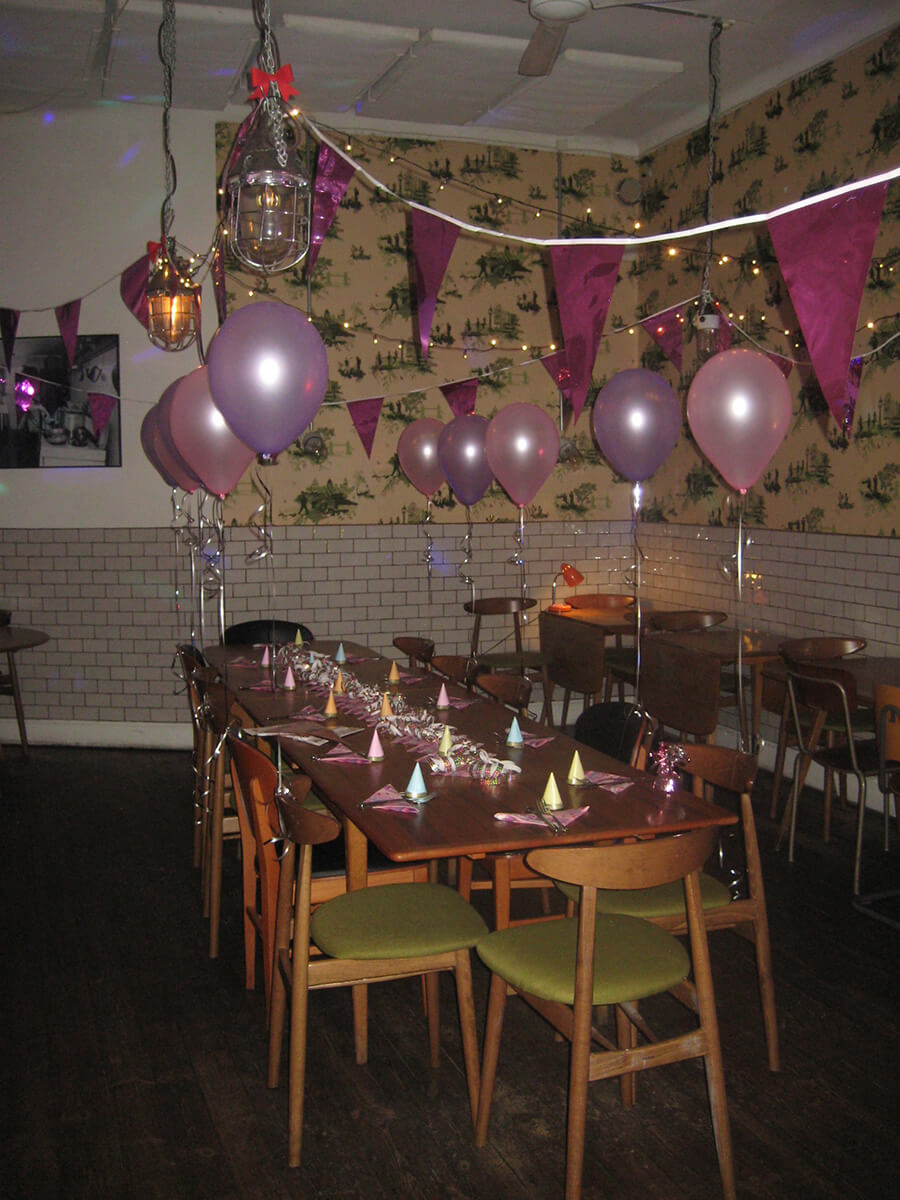 Large table with chairs in a room that is decorated with pink and purple baloons and streamers