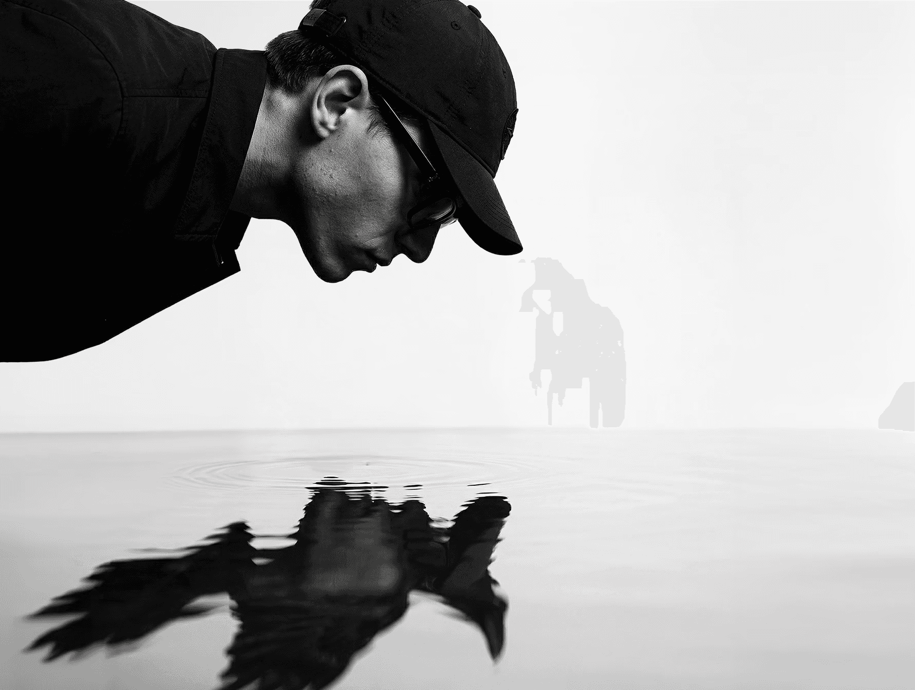 Black and white conceptual self portrait by Théodore Deslarzes exploring identity through water reflection and symbolic raven imagery.