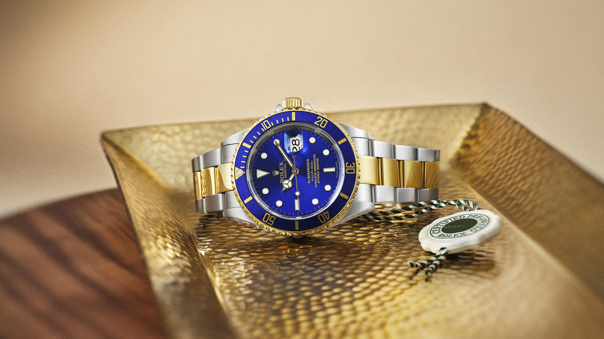 A stylish rolex watch with a blue face and silver band, resting on a golden surface.