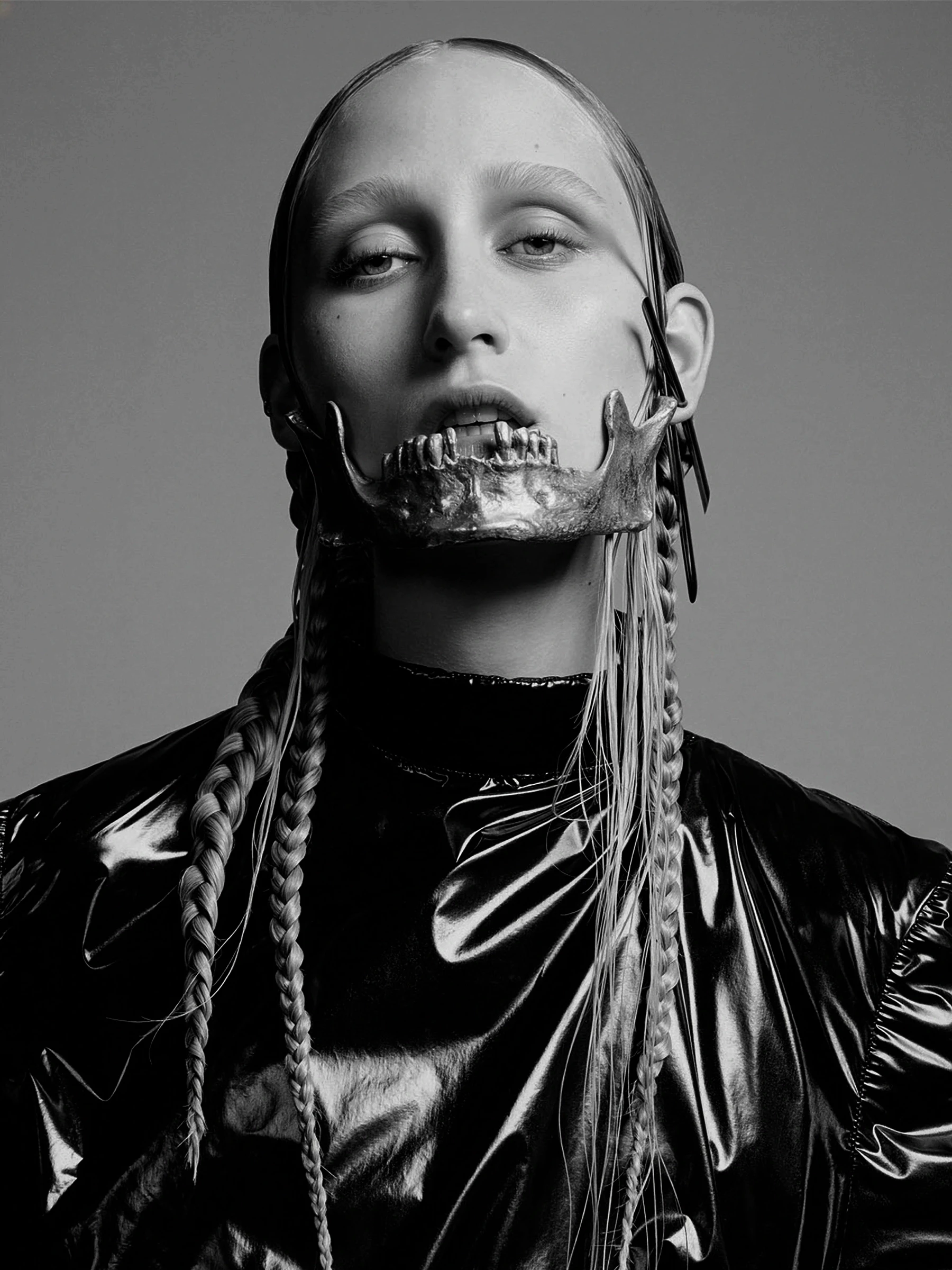 Avant-garde silver skull jaw piece by Shaun Leane worn over the lower face, paired with a glossy black high-neck jacket.