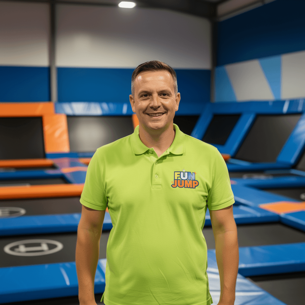 A young person with curly hair smiles at the camera while sitting in front of a laptop against a dark background.