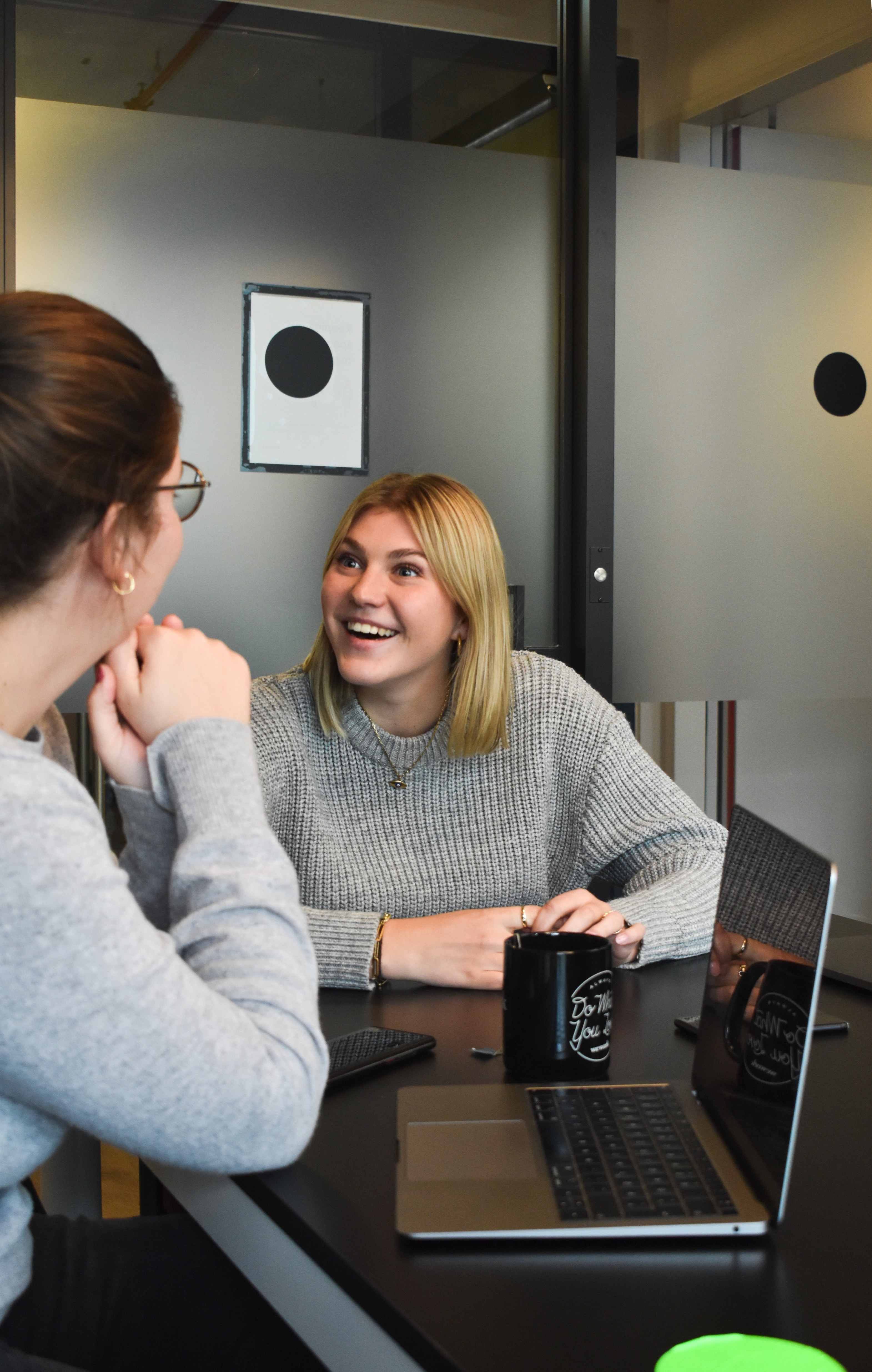 A woman sat at a table smiling at another woman in front of a laptop
