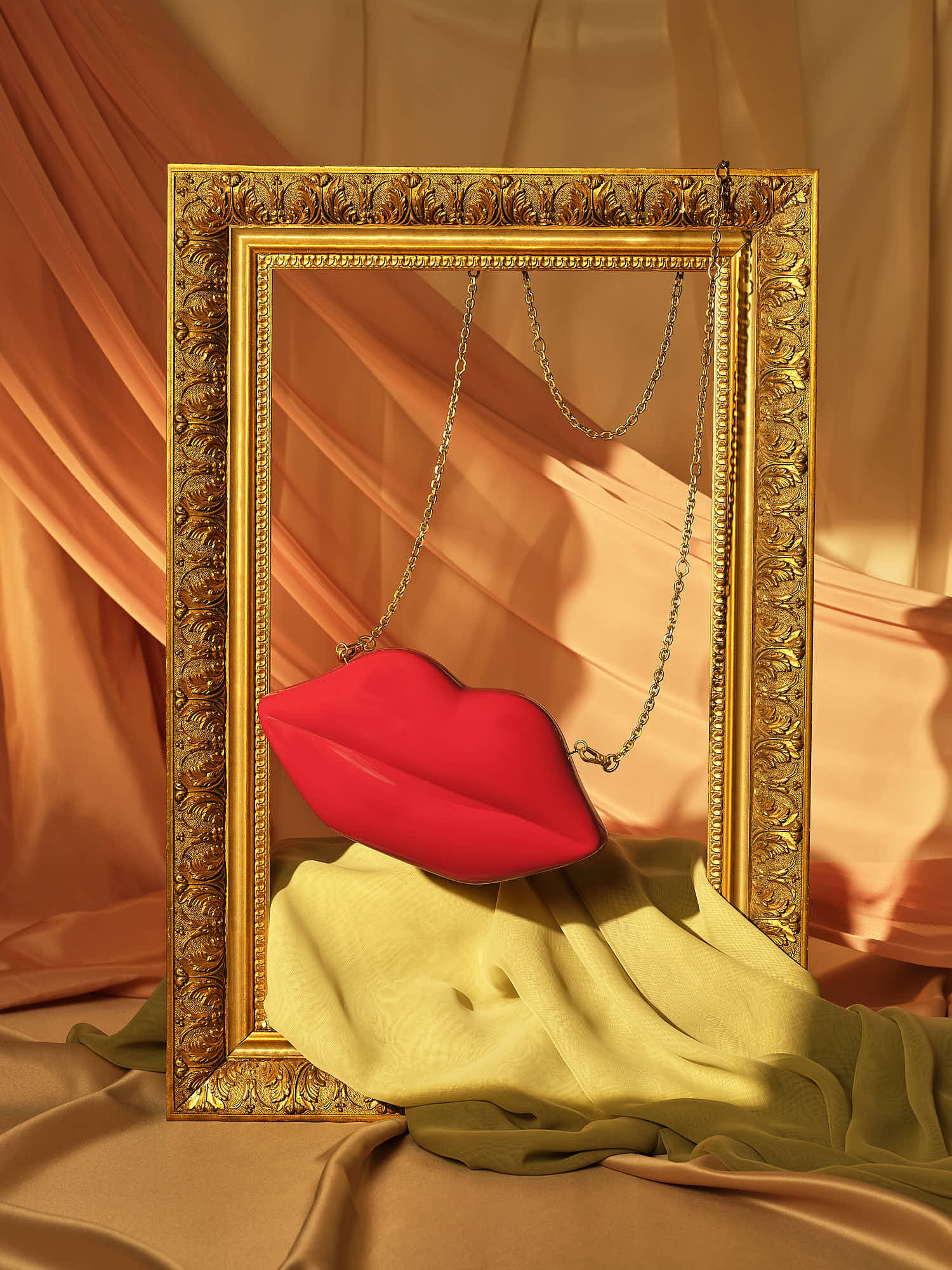 Gold ornate frame with hanging red lips sculpture on draped fabric backdrop.