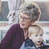 Elderly woman holding a young child outdoors, both looking attentively in the same direction.