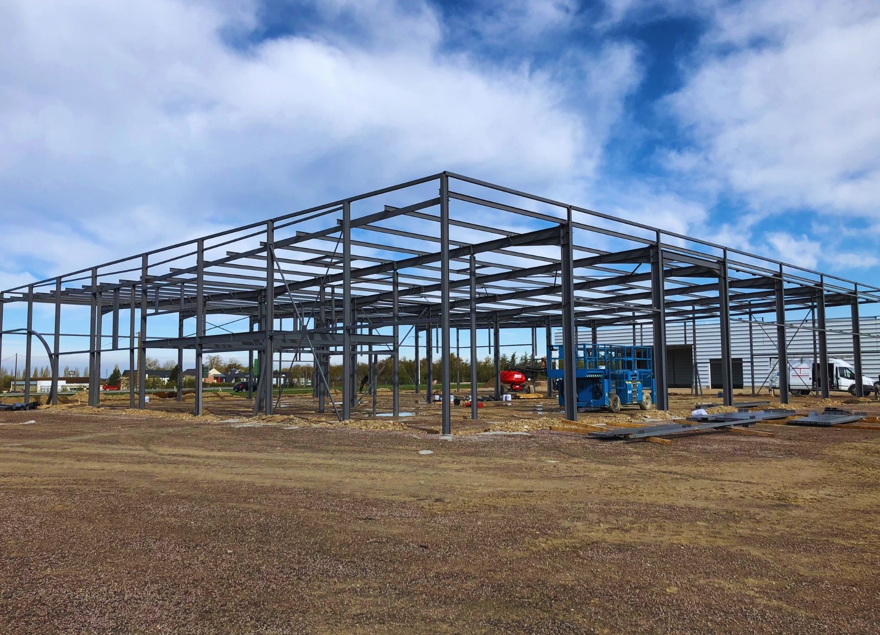 Chantier de construction avec ossature métallique en cours d’assemblage sur sol stabilisé.