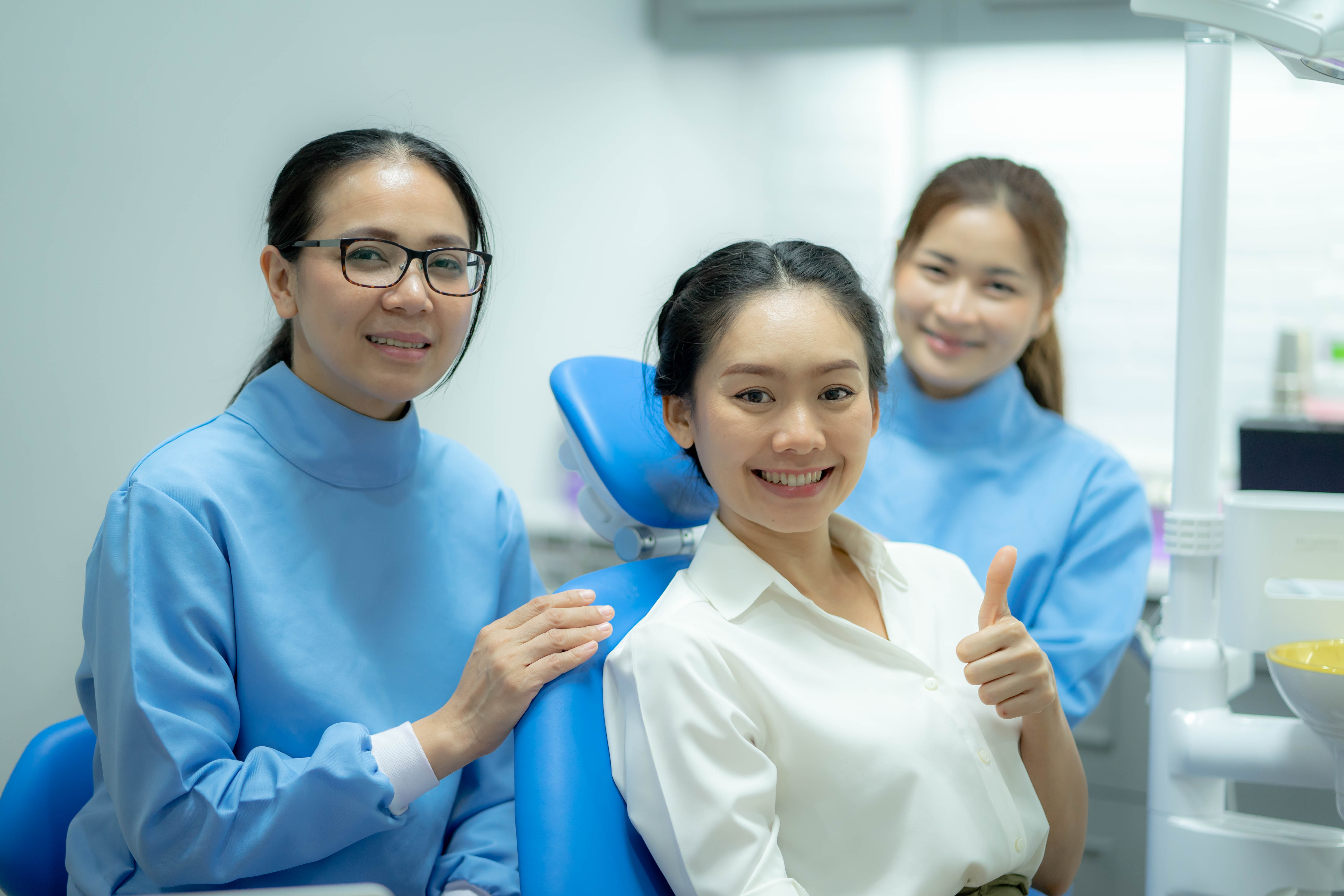 A dental professional wearing protective gear and a mask performing a dental procedure on a patient lying in a dental chair.