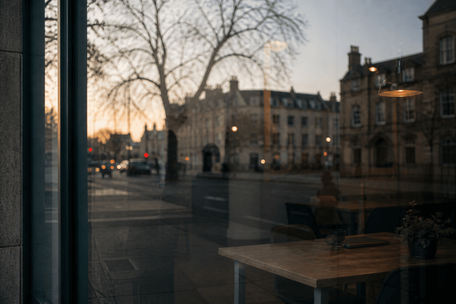 Reflections of a Cambridge street seen through a window at early evening, blending outdoor buildings with a softly lit interior space.