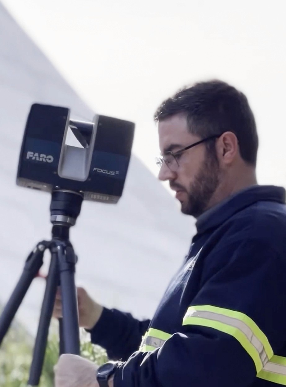 Close-up lateral de um técnico operando um scanner a laser profissional da marca Faro montado sobre um tripé. O equipamento é utilizado para a Captura da Realidade de alta precisão, gerando nuvens de pontos detalhadas do ambiente construído.