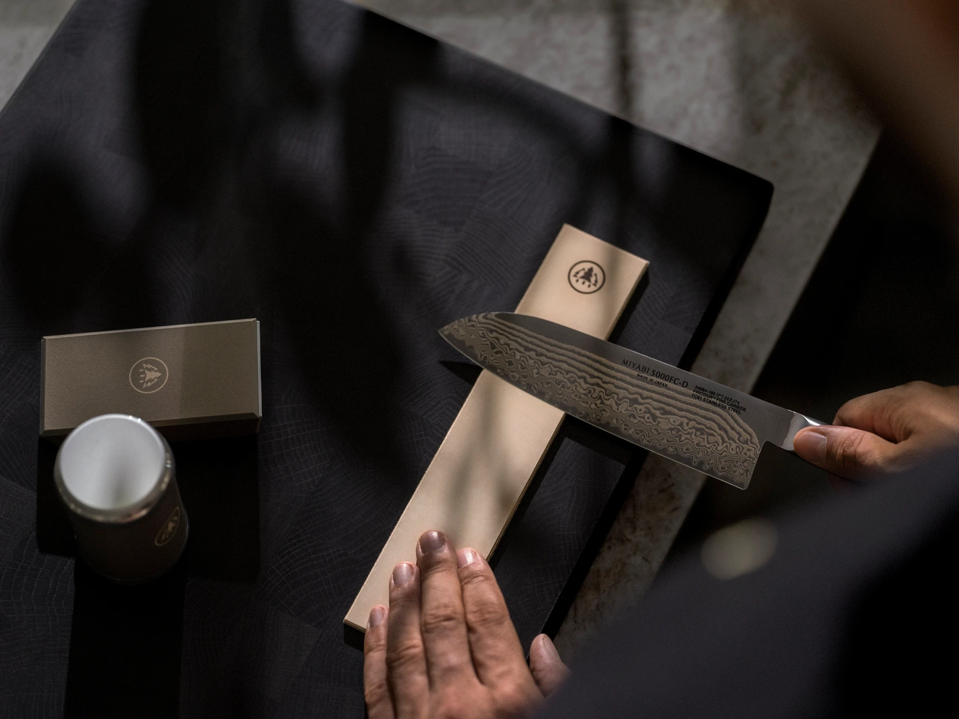 A hand carefully stropping a Damascus steel knife on a leather surface to achieve a polished, razor-sharp edge.