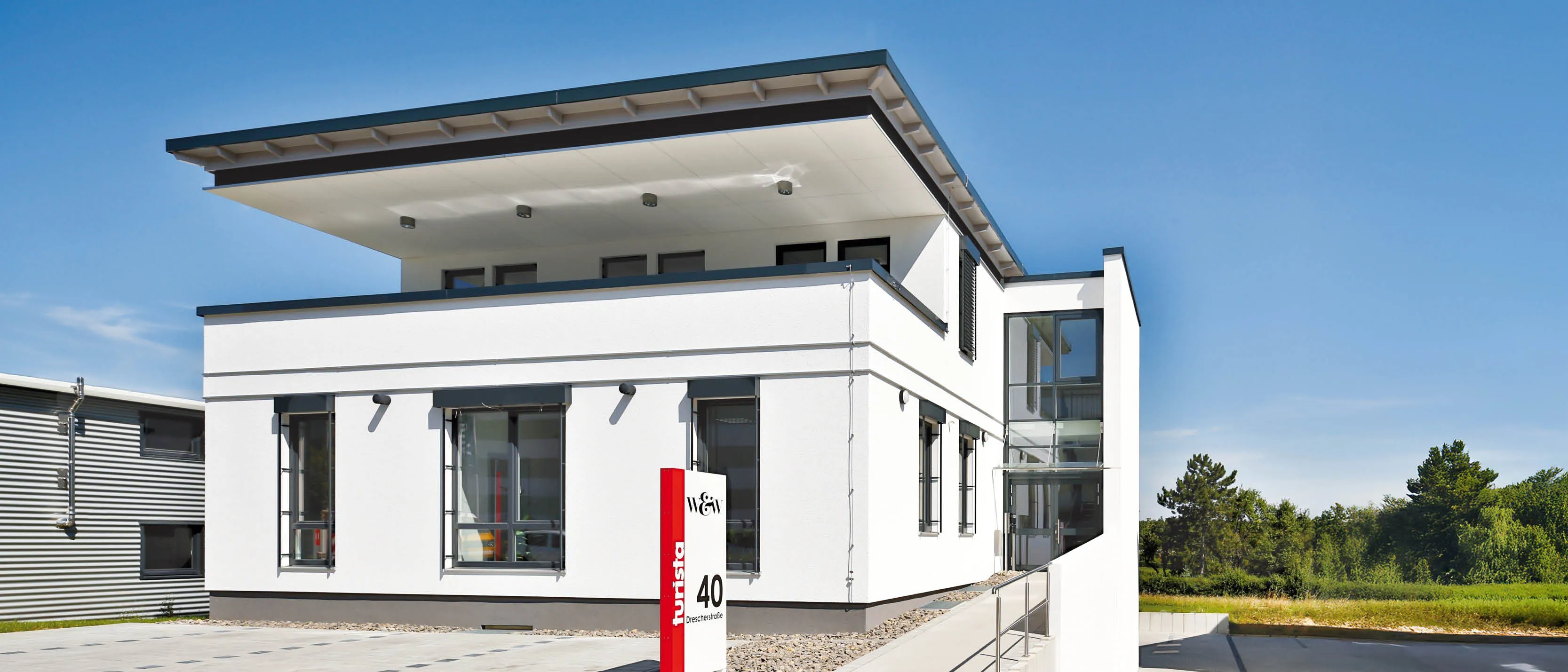 Moderne weiße Bürogebäude mit Glasfront, Unterführung und Beschilderung, daneben Lagerschuppen.