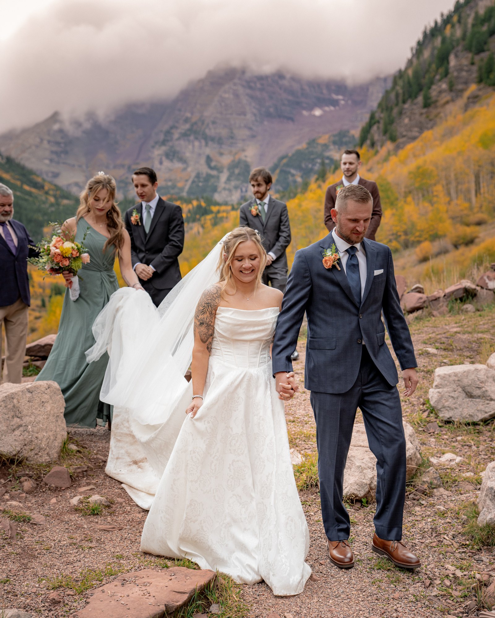 Newlyweds walking away from their Maroon Bells ceremony with their wedding party behind them