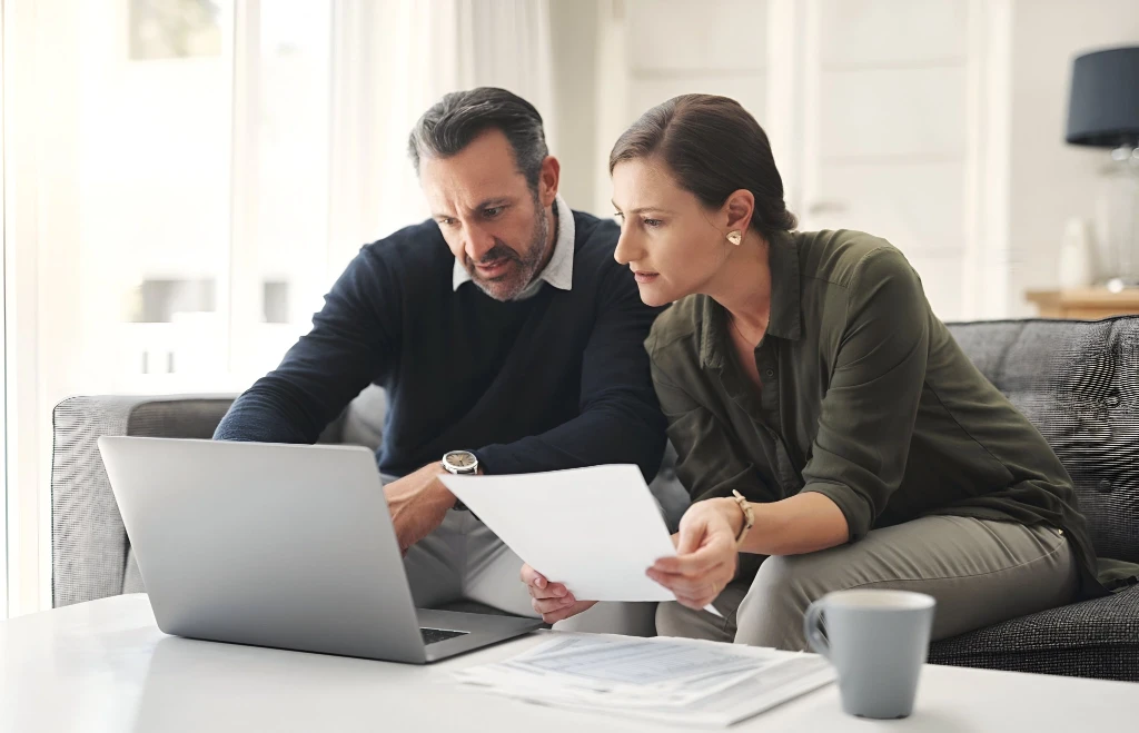 Mature couple looking at laptop reviewing documents.