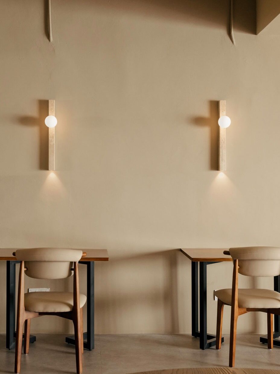 Interior view of a co-working space with wooden tables and light-colored walls, featuring stylish wall lamps and minimalist chairs.