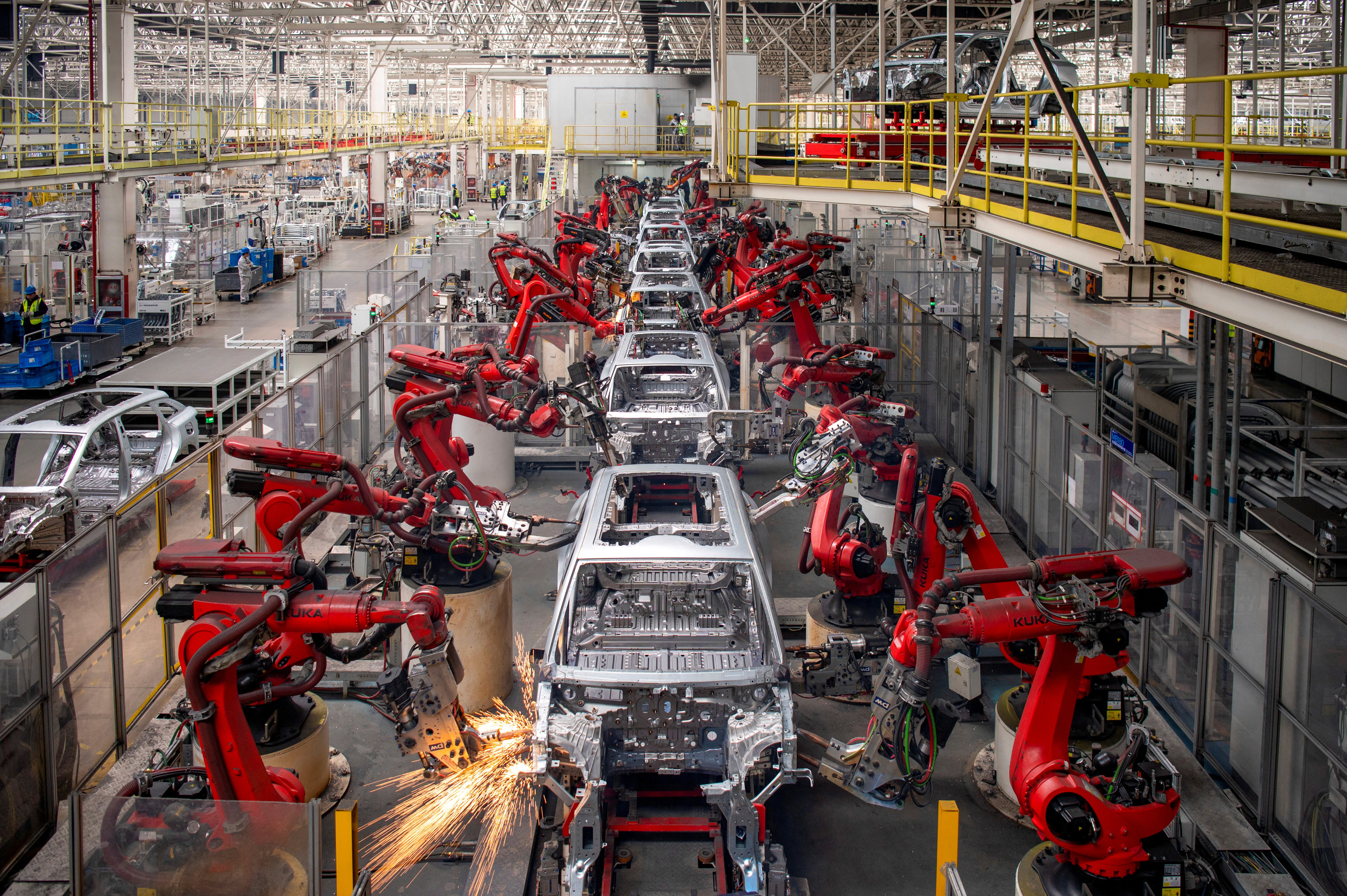Two people in a workshop, one standing and smiling while the other leans over a car, working on it.