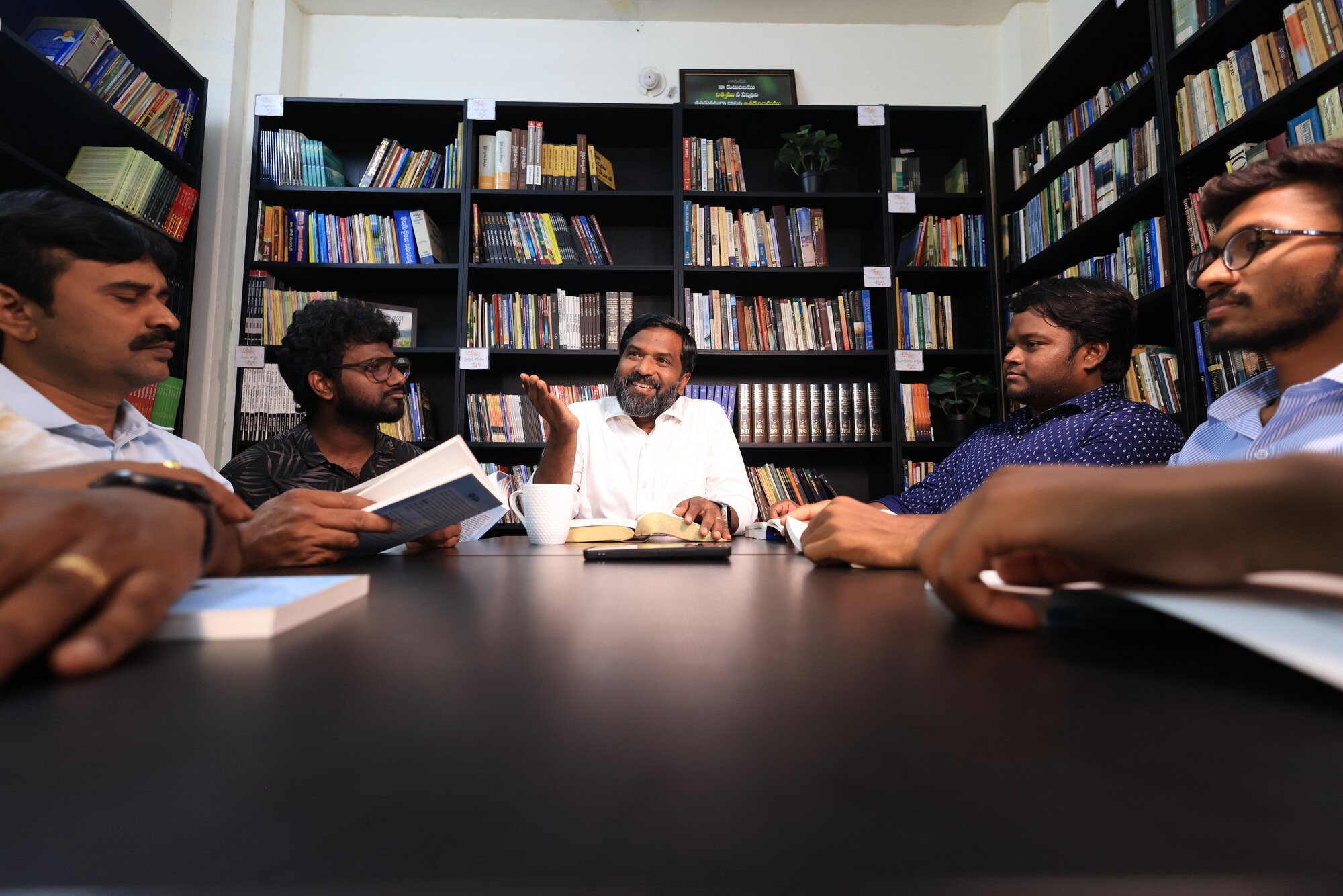 A man teaching from an open book at the head of a library table