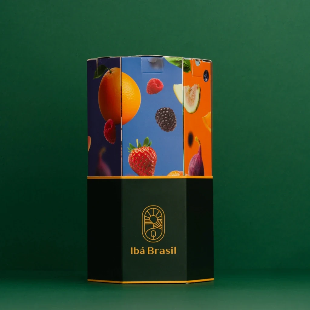 Caixa hexagonal Ibá com a arte de frutas — laranja, morango, amora e figo — sobre fundo verde.