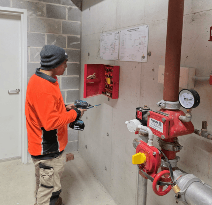Technician in hi-vis drilling beside a fire sprinkler valve set