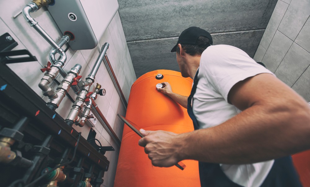 A heating engineer making adjustments on a large orange boiler