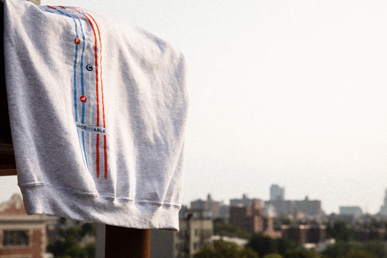 Close-up of Staple x NYCFC hoodie detailing with orange and blue stripe accents on fabric.