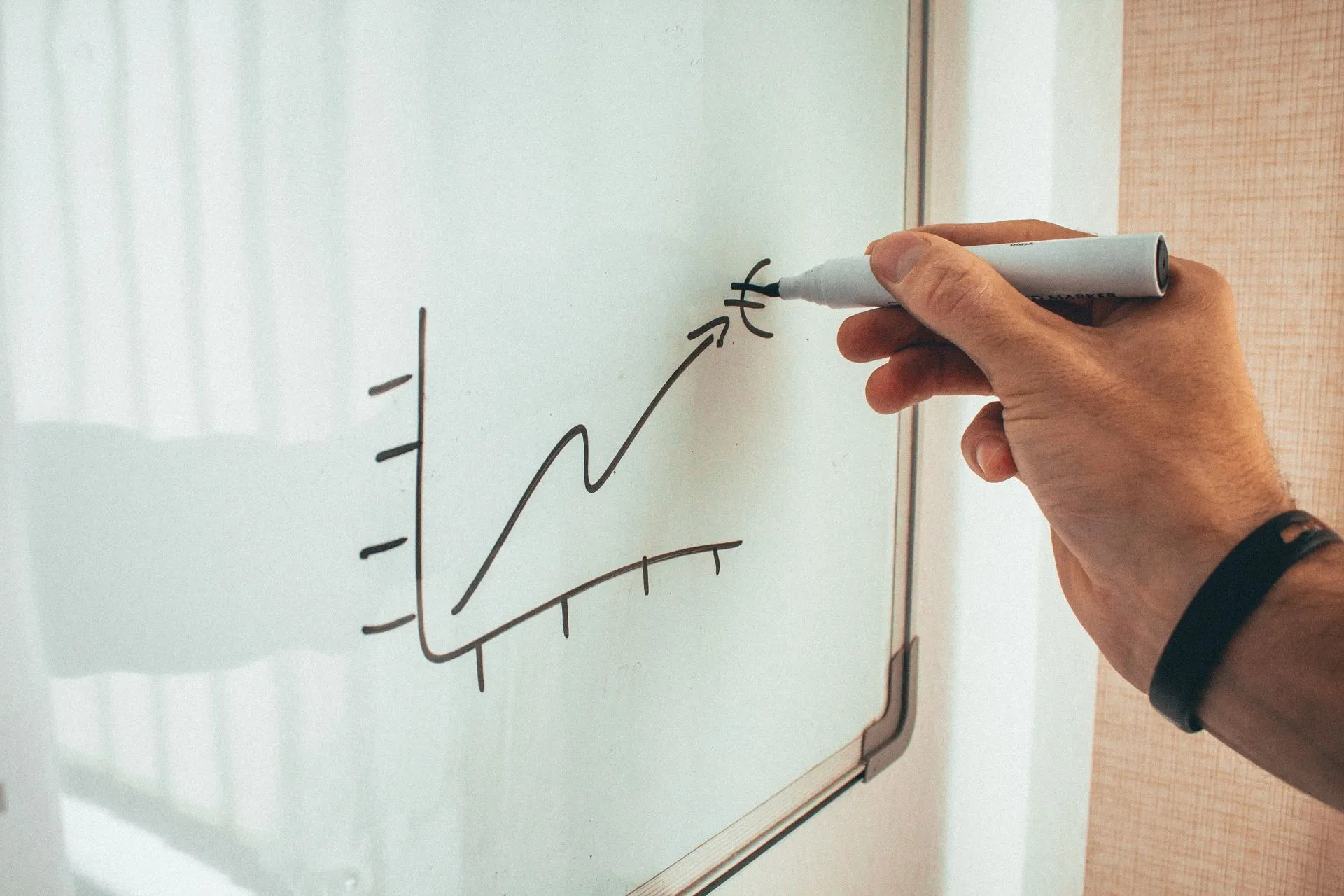 Hand drawing an upward growth chart with an arrow on a whiteboard