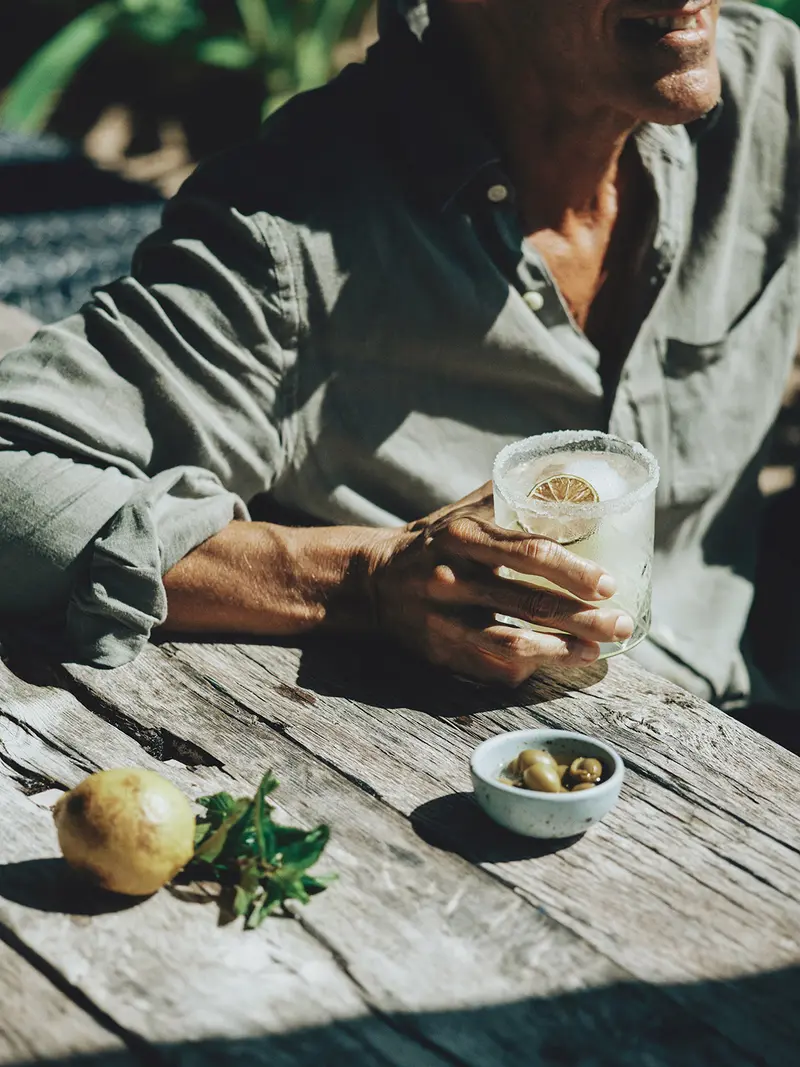 Man holding a glass with a prepared drink, garnished with a lemon slice and ice, at Jungle Bar, Be Tulum.