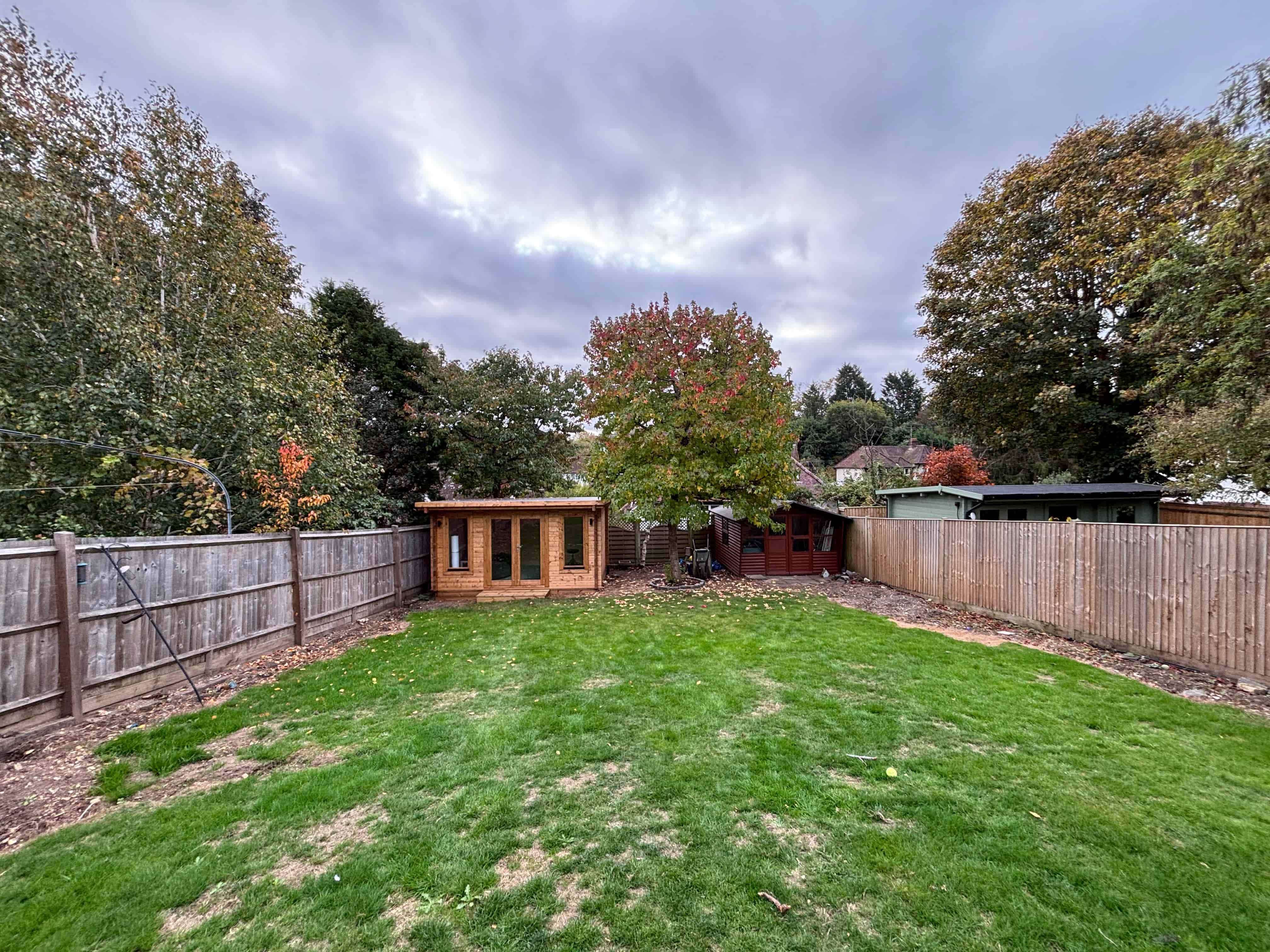 : Garden path through modern black wooden pergolas leading to a green shed.