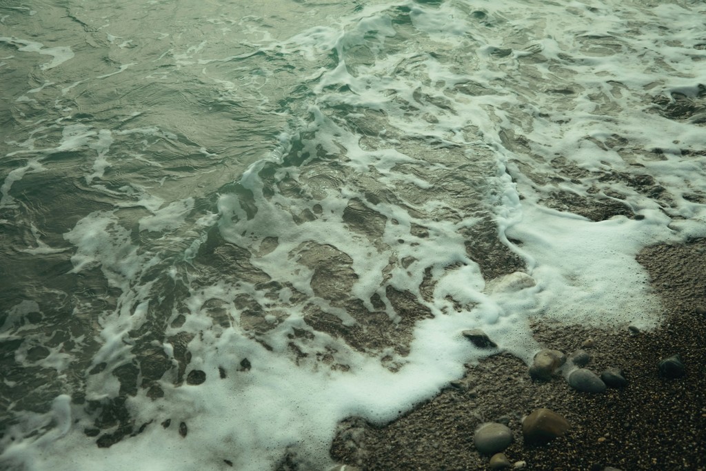People are working and walking in a modern office space with wooden floors, large windows, and various seating arrangements.
