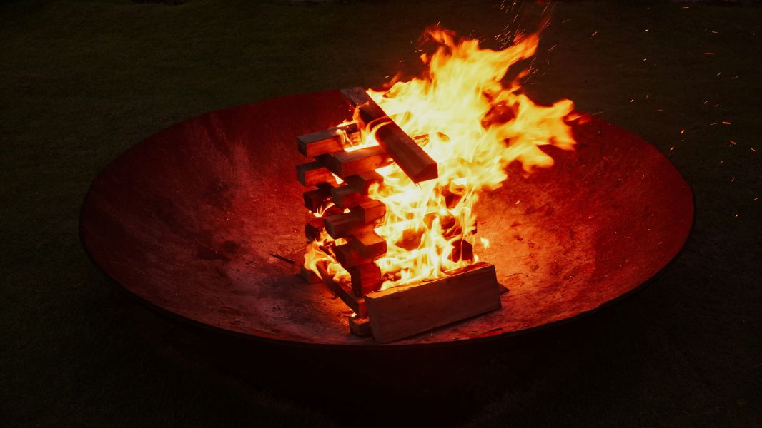 A roaring campfire burns in a large red fire pit.