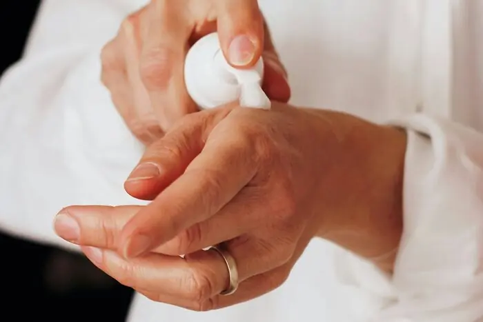 Hands smoothing lotion dispensed from a white pump bottle