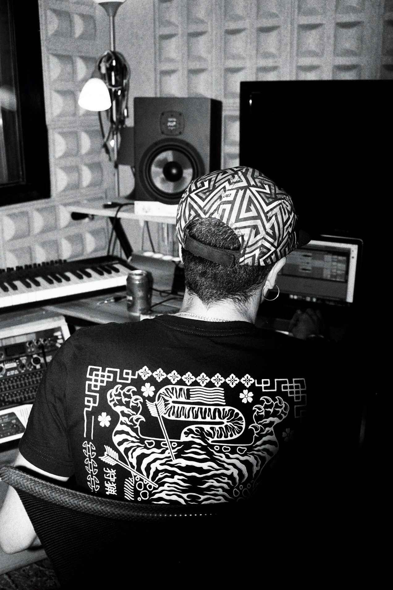 A person with a cap sits at a music studio, focusing on equipment with vintage decor in black and white.