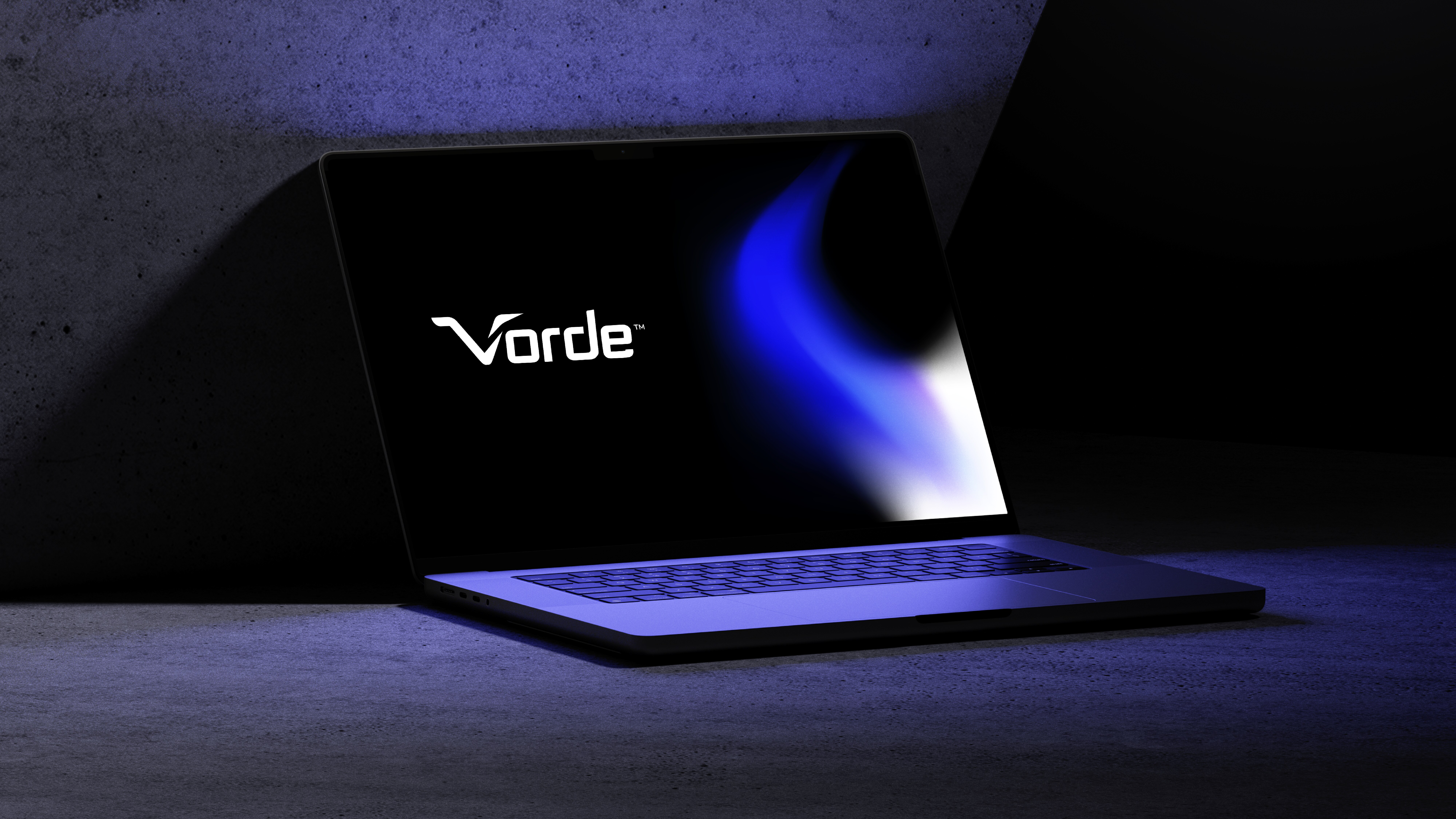 A laptop showcasing the word "Vorde" against a blue and black screen sits gracefully in Manasi Doshi's studio, its sleek design contrasting with a concrete backdrop.