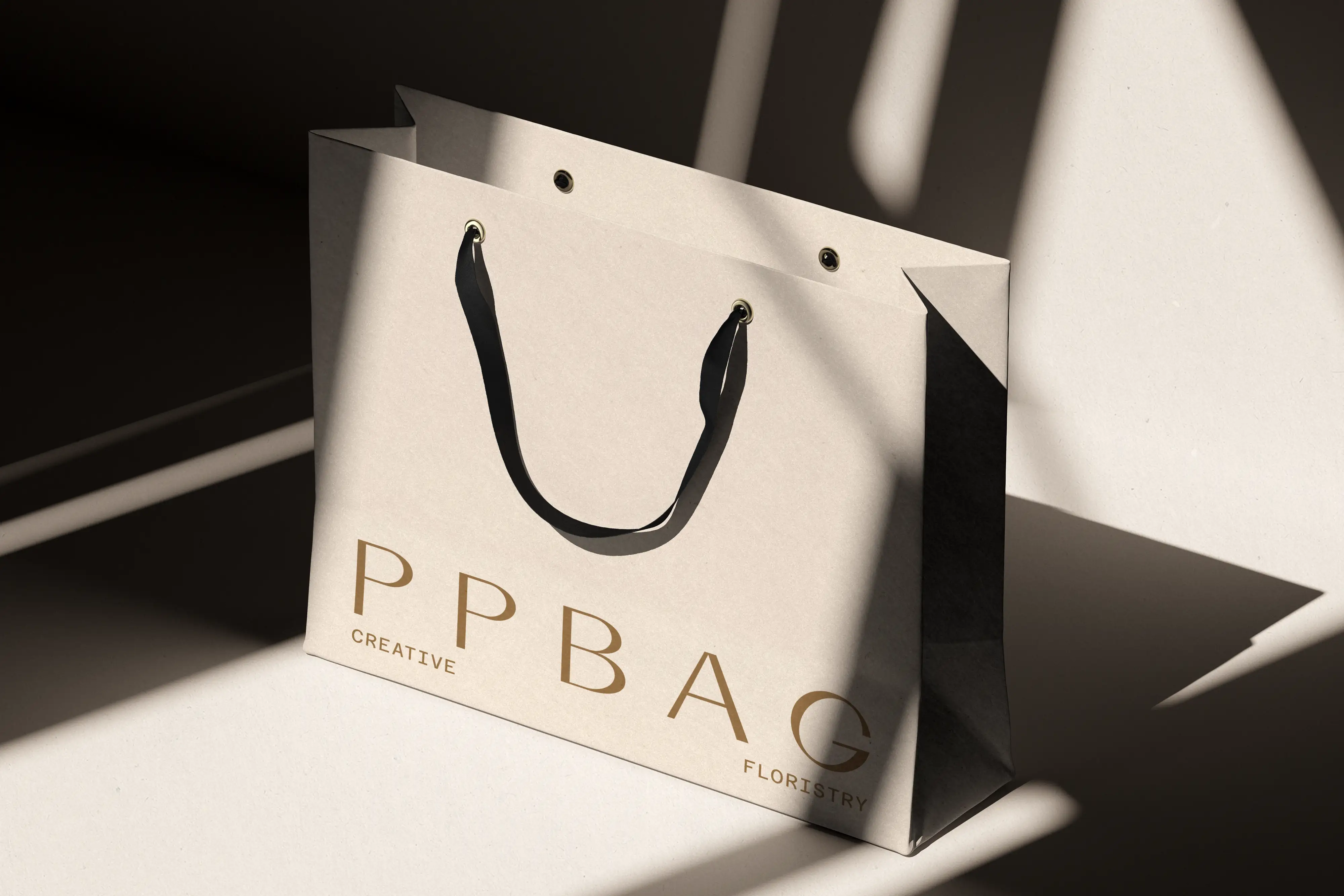 Cream paper shopping bag with gold wordmark and hard shadow