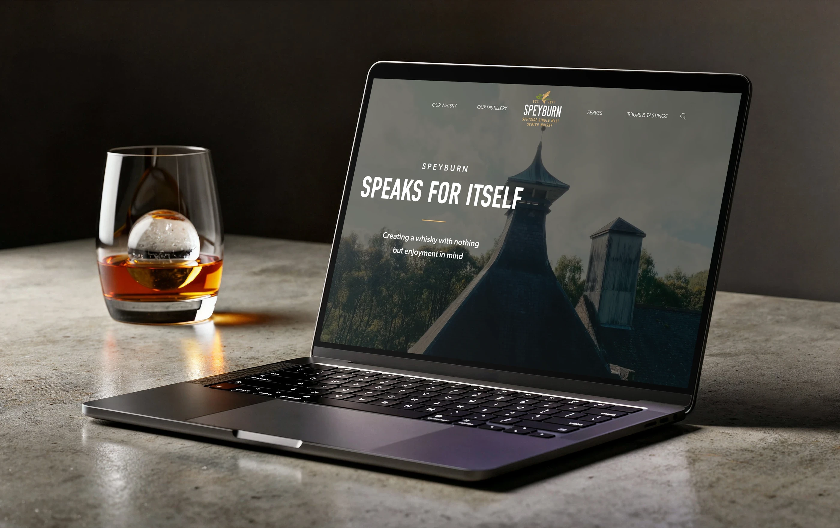 Laptop with Speyburn Whisky homepage on screen sitting sitting next to glass of whisky