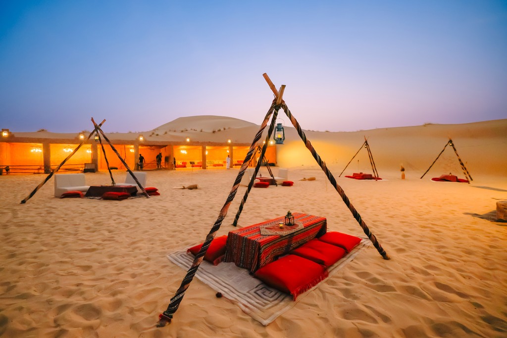 A group of professionals seated in a traditional Bedouin-style setup in the UAE desert, attending a corporate event organized by Sparkling Sandset. The golden sand dunes, black-and-white striped tents, and Arabic seating arrangement create an authentic desert camp ambiance. The event blends culture and business, showcasing Sparkling Sandset’s expertise in managing premium corporate events and desert experiences in Abu Dhabi and Dubai, UAE.