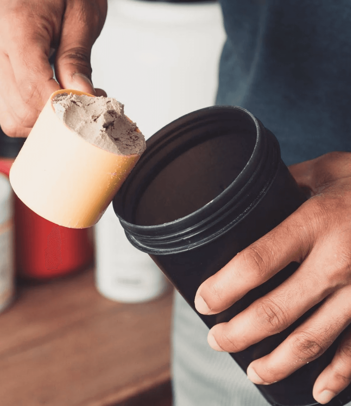 Person preparing a supplement drink with a scoop and shaker bottle.